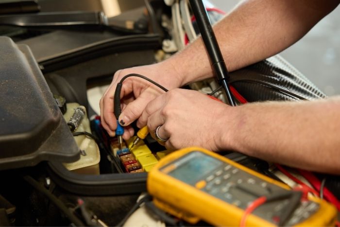 Mechanic using a multimeter to test electrical components under the hood of a vehicle.