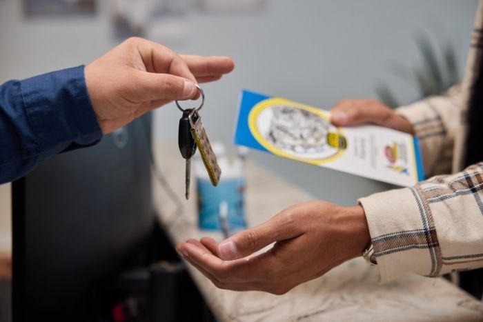 Close-up of a key exchange between two people, one holding car keys and the other receiving with an info brochure.