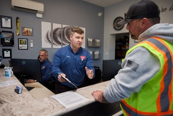 Customer service interaction with a staff member explaining paperwork to a man wearing a neon safety vest and cap.